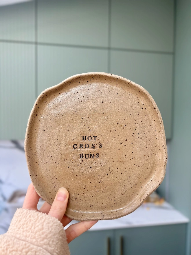 A wavy plate in speckled clay being held up in a kitchen. 