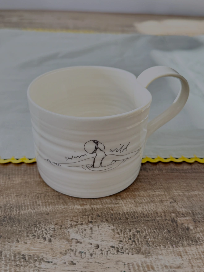 Handcrafted porcelain ‘Swim Wild’ mug – unique ceramic coffee cup for swimmers, nature lovers, and outdoor adventurers.