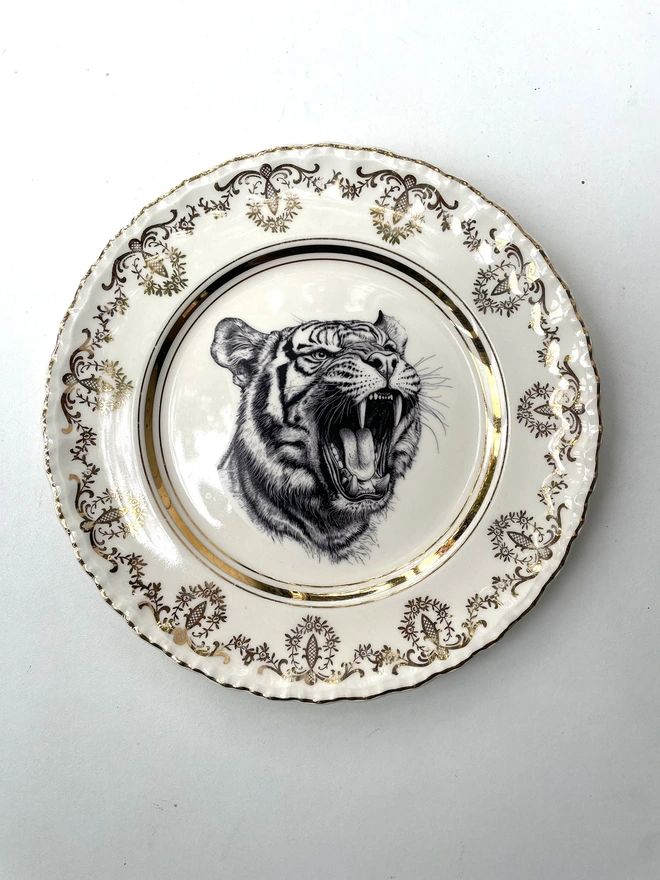 a vintage plate with an ornate border, in the centre of the plate is a vintage style black and white illustration of a tiger roaring