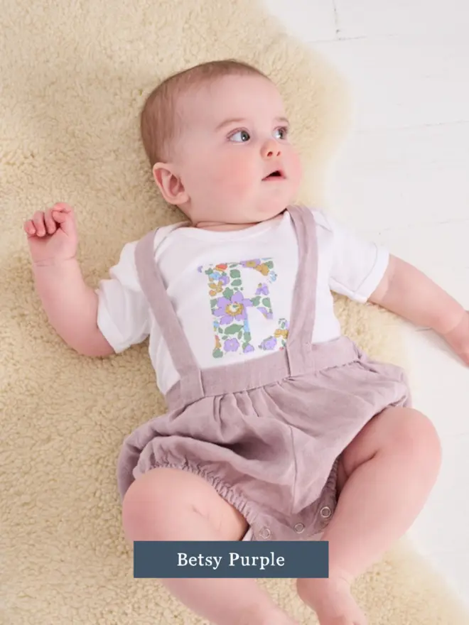 a baby wearing a personalised cotton bodysuit with her initial on in floral betsy liberty print