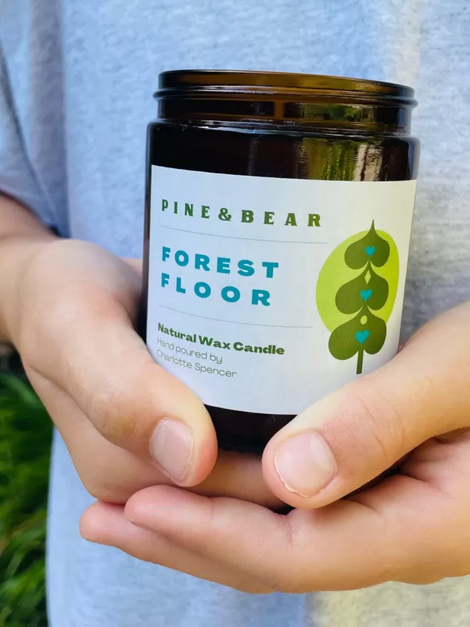 Natural wax forest floor candle being held in a gilrs hands.