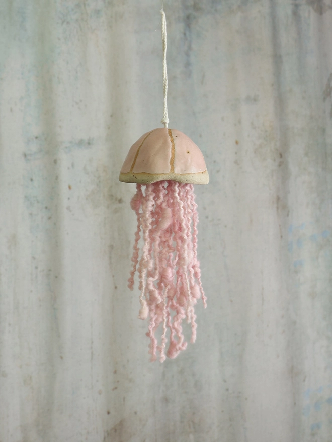 pale pink handmade jellyfish hanging hangs by itself infront of a grey toned backdrop