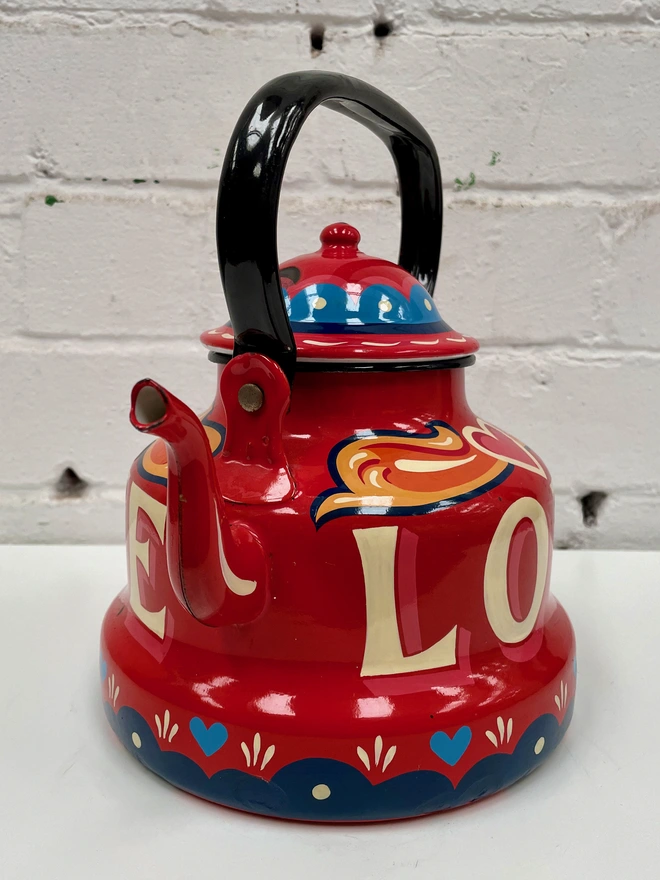 Red vintage enamel kettle, hand-painted with a fairground inspired design in orange, pink, yellow and blue. 'Love' is painted in large lettering across the centre.