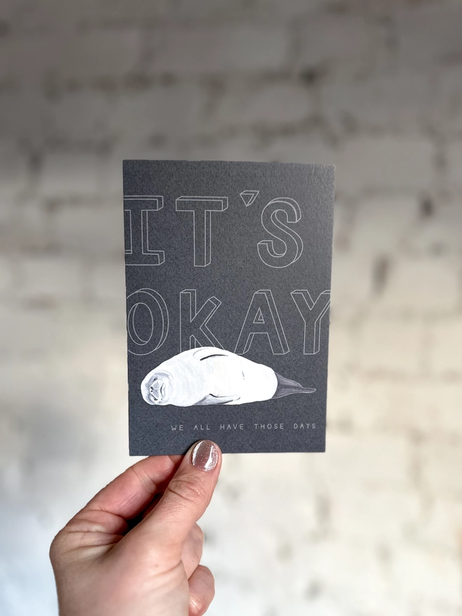 a dark grey greetings card featuring an illustration of a seal with the text “It’s Okay - we all have those days”