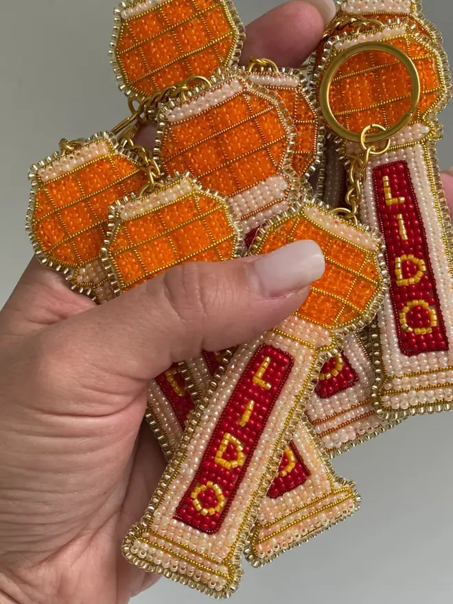 Multiple beaded lido key rings with orange, red, and beige beads held in a hand, against a plain background. 