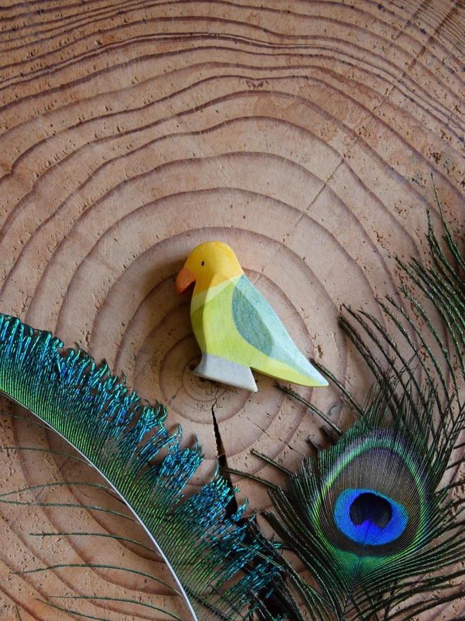 wooden toy lovebird on wood slice with peacock feathers