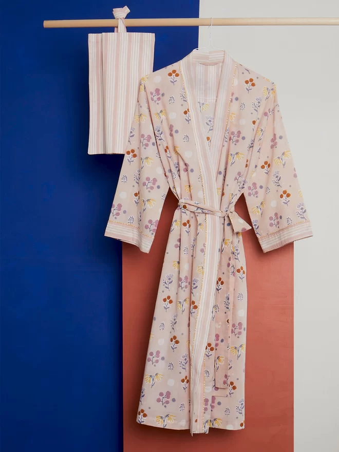 Block printed floral dressing gown and matching bag hanging on wooden pole in front of a tan and bright blue background 