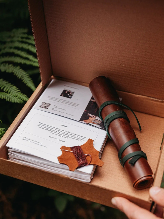 make your own leather journal. an open cardboard box containing components for a DIY leather journal kit.