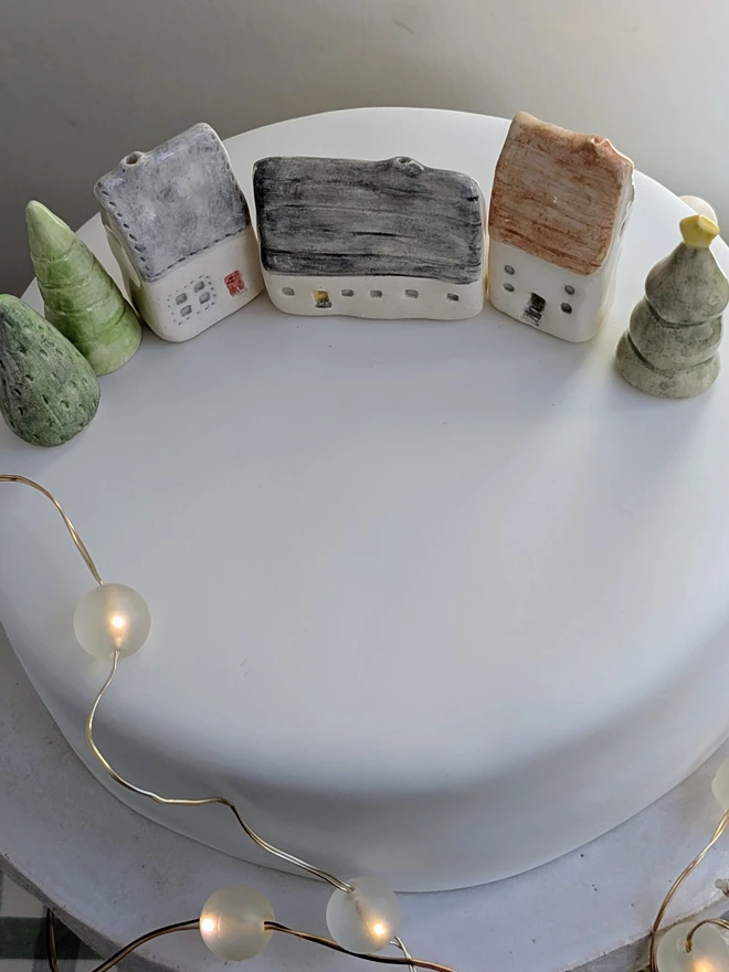 miniature ceramic house and tree cake topper ornament on a white Christmas cake