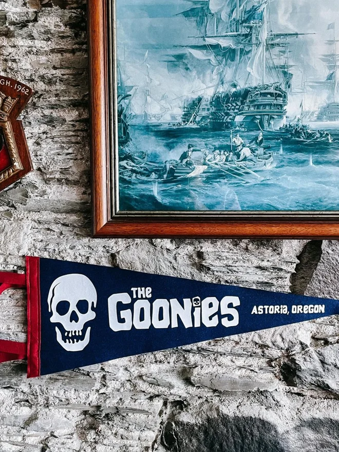 a navy and white felt pennant with a skull on and the words The Goonies