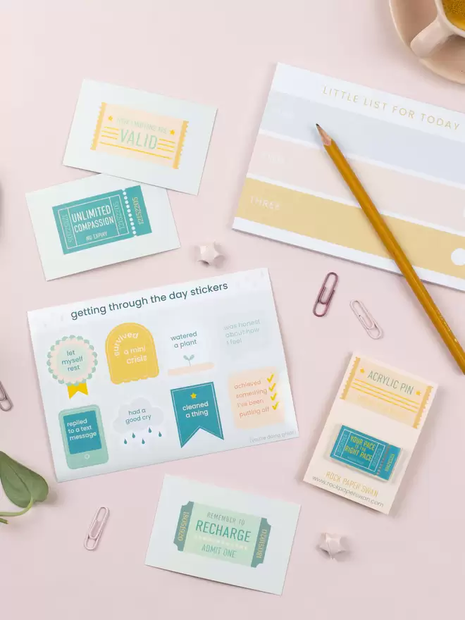 Flat-lay of co-ordinated stationery that includes a sticker sheet, notepad, pin badge and mini cards.