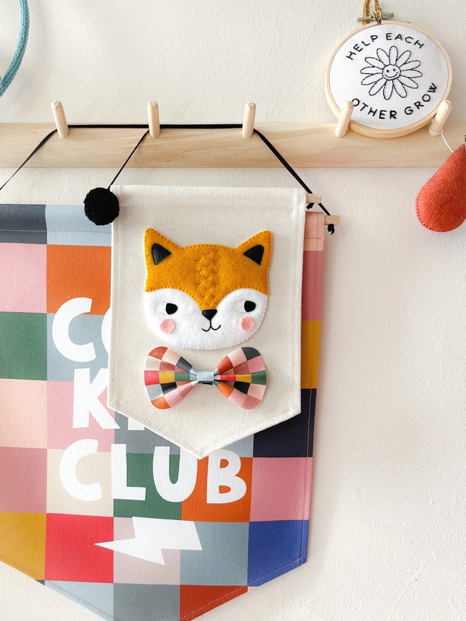 Hand sewn fox banner hanging from a wooden peg rail