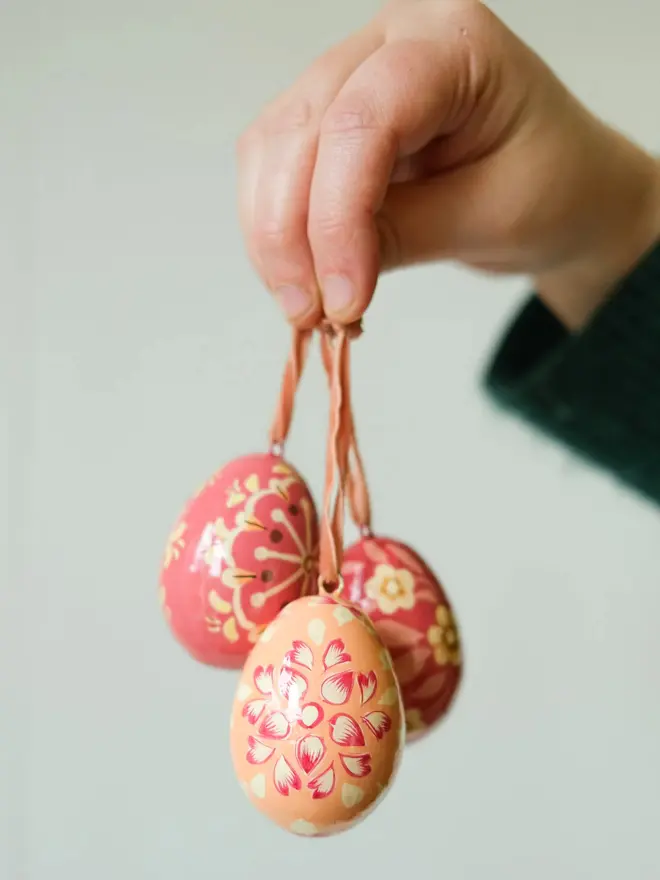 Group shot of hand painted decorative eggs on velvet string held up by a hand