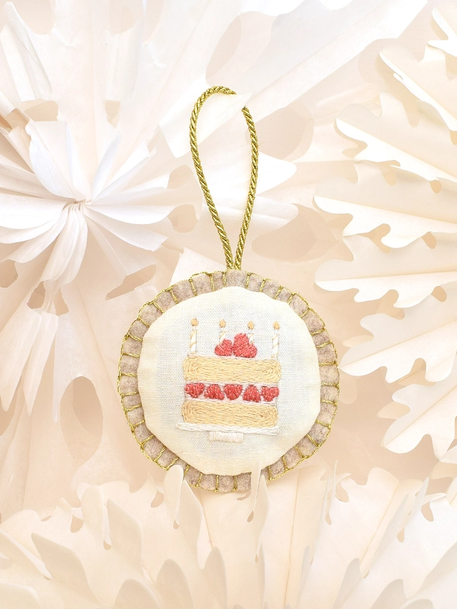 The finished Birthday cake embroidery turned into a felt bauble, displayed amongst paper-cut stars.