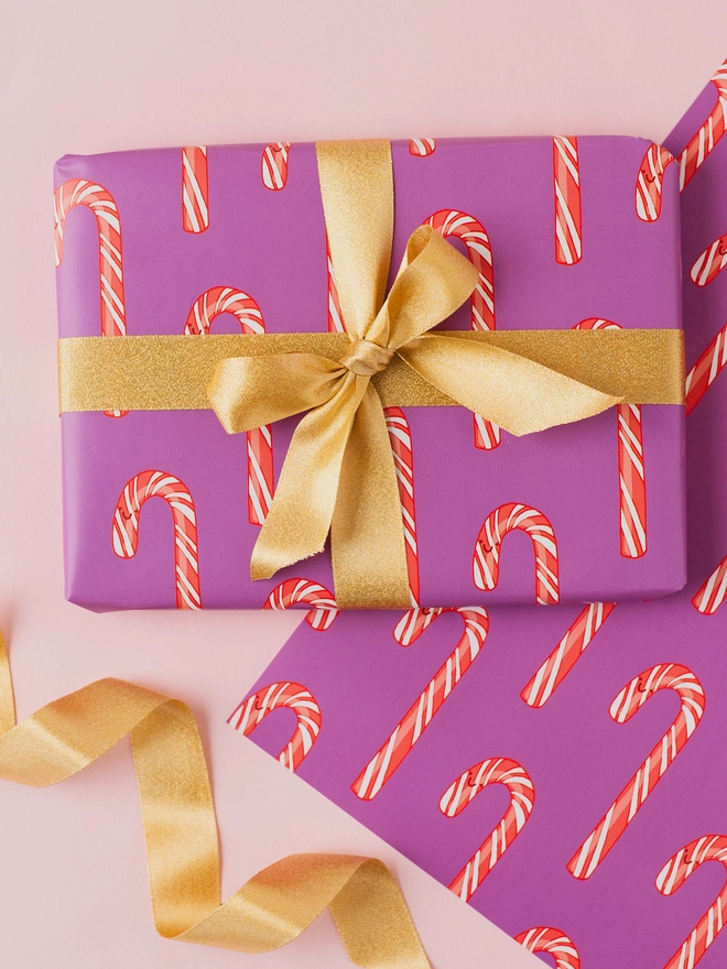 Purple Christmas wrapping paper featuring a repeating pattern of hand-drawn red and white striped candy canes.