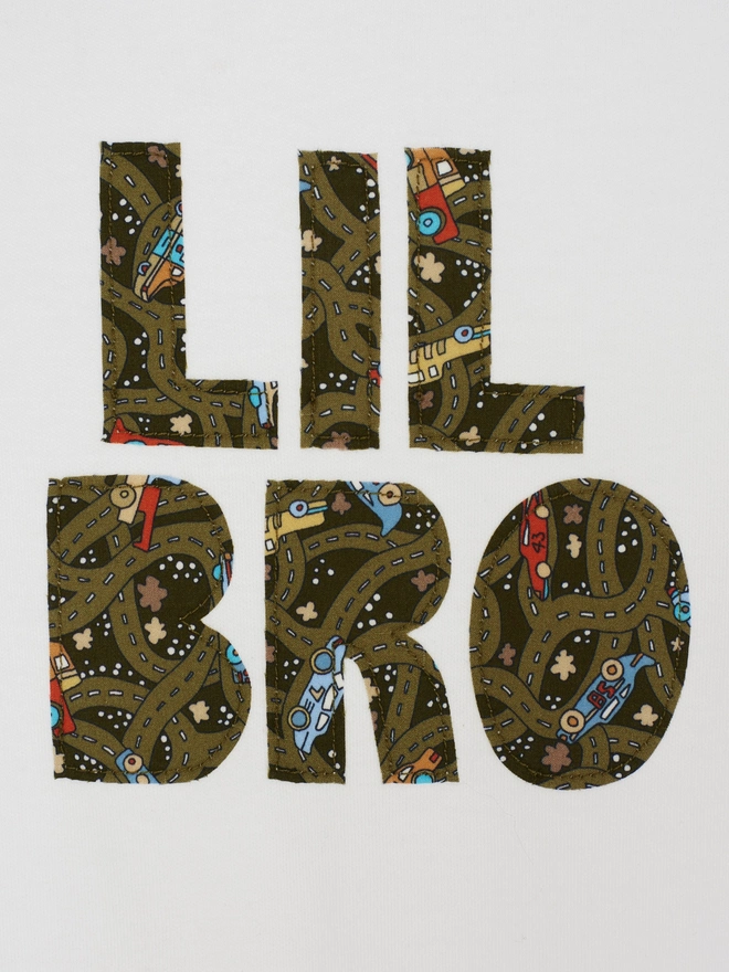 Lil Bro appliquéd on a white cotton baby romper in a vintage cars and busses Liberty print. A close up of the stitching