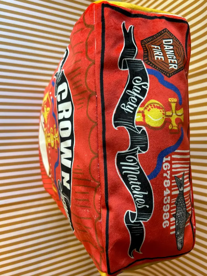 Crown Matchbox Cushion, a colourful red cushion sitting on a decorated surface. 