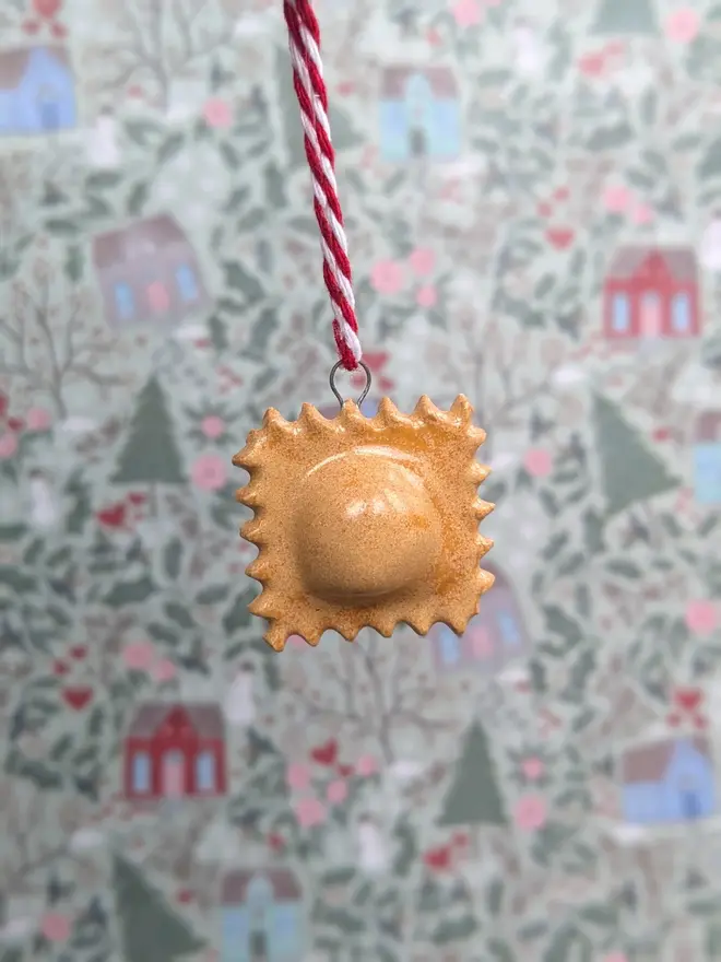 ceramic ravoilini christmas decoration. a small pasta ornament hanging from red and white thread.