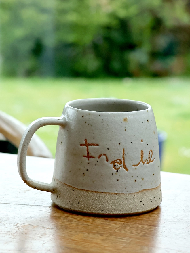 Personalised Kids' Handwriting Handmade Stoneware Mug on a wooden table featuring the name 'Indie'