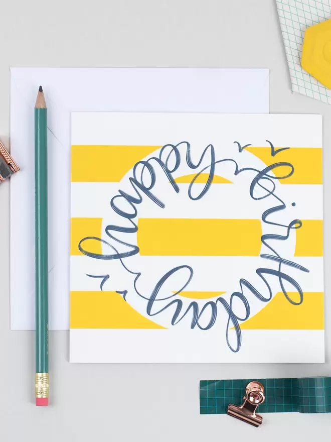 A yellow-and-white striped card which reads 'happy birthday' in blue hand-lettered circular script