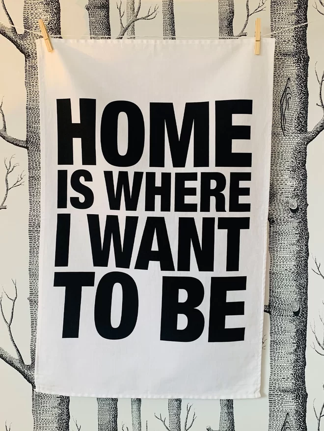 London Drying Home Is Where I Want to Be black text on white tea towel hanging washing line style in front of black and white silver birch tree woods pattern wallpaper 