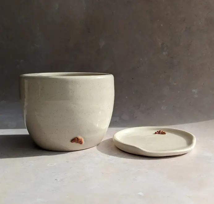 Vanilla bean–colored croissant coffee cup with a subtle croissant design, placed against a grey marble background.