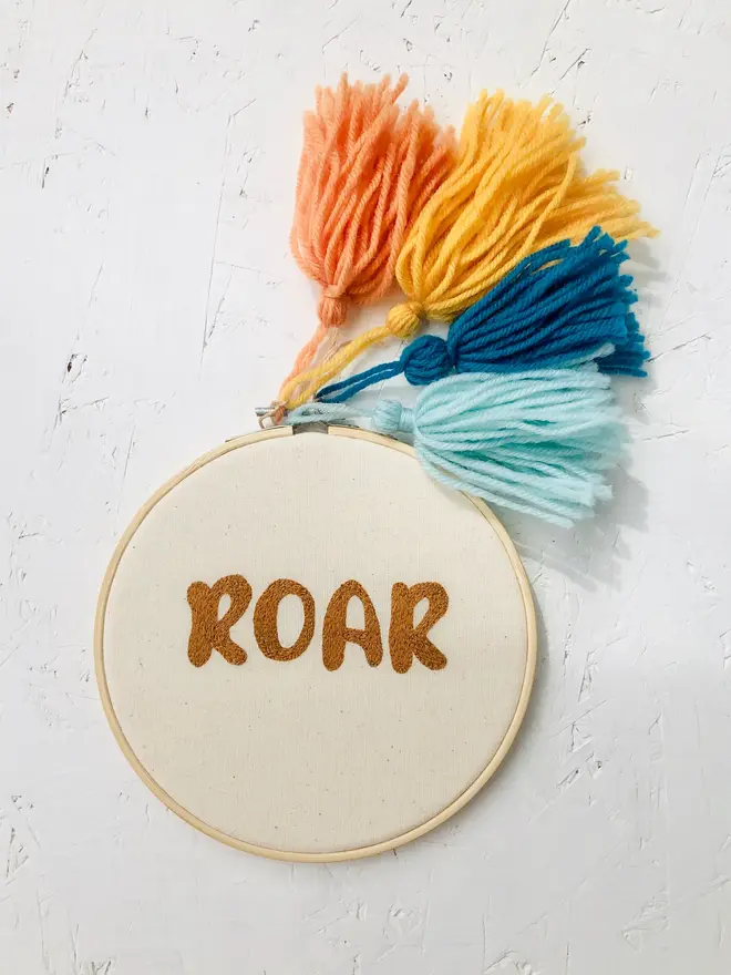 custom phrase embroidered hoop. cotton hoop embroidered with 'roar' in orange lettering.