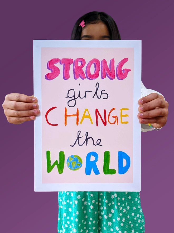 Young girl standing holding an art print saying 'Strong girls change the world'
