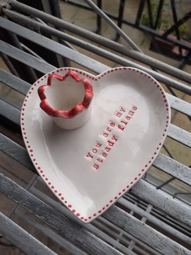 Handcrafted white ceramic heart candle dish with a ruffled red candle holder rim and red dotted border, designed for a dinner taper candle.