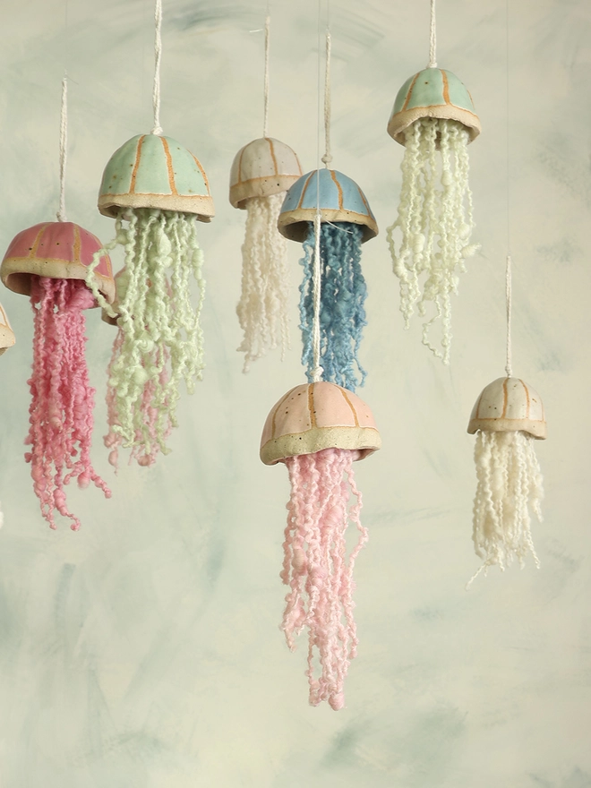 handmade ceramic jellyfish with wool tenticles hang at various heights, the hanging jellyfish decorations are in bright pink, pale pink, green, blue and white.
