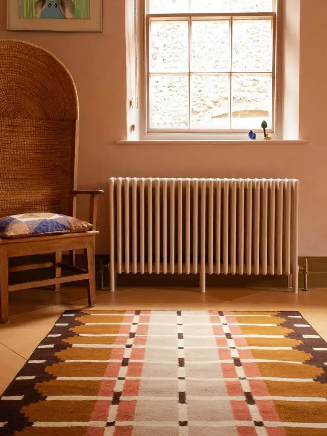 Corbie Flatweave Rug, a colourful rug sitting in a decorated room. It is accompanied by other household items. 