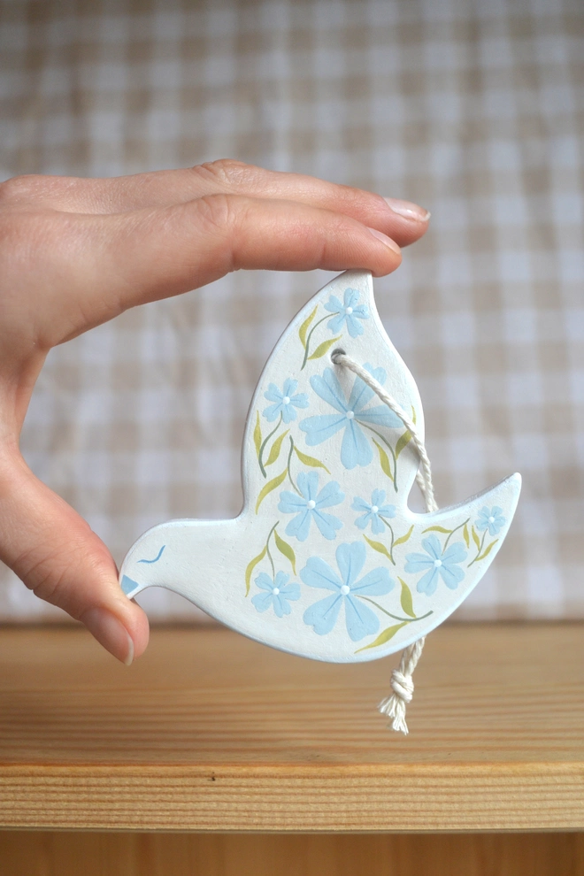 white ceramic hanging bird with blue and green floral designs, in front of gingham 