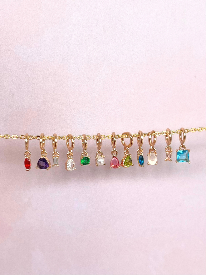 hanging mini birthstones charms on fine gold chain on a pink background