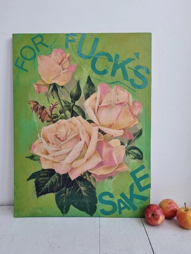 A painted plywood panel in green featuring decoupage of three large peachy pink roses taken from a Victorian seed packet with a motivational phrase that reads for fuck’s sake.