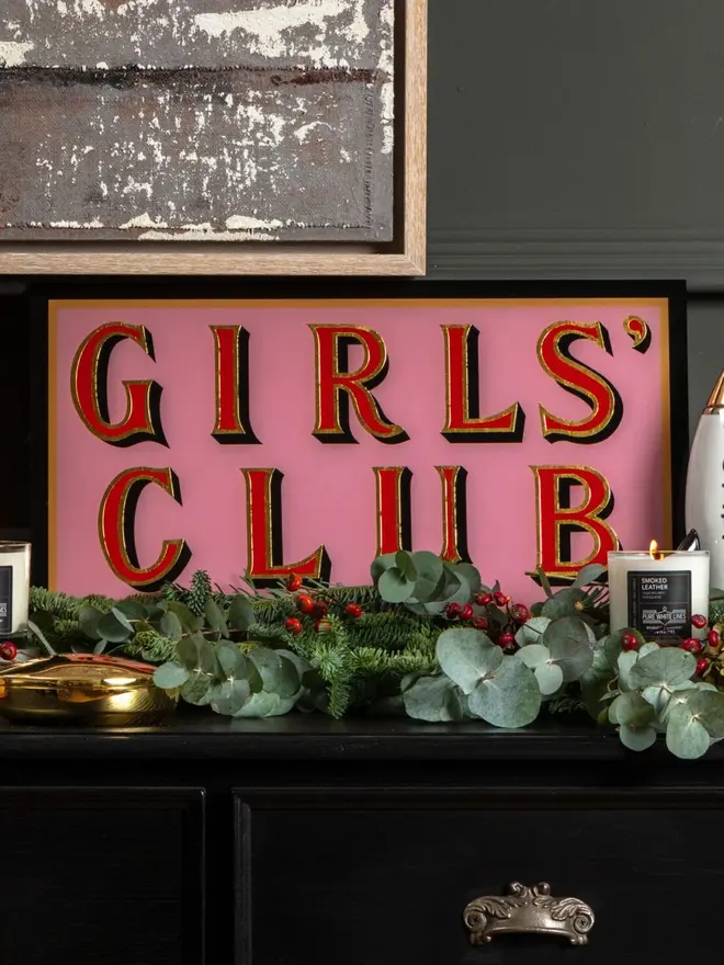 girls club pink hand painted sign. sign propped up on mantelpiece.