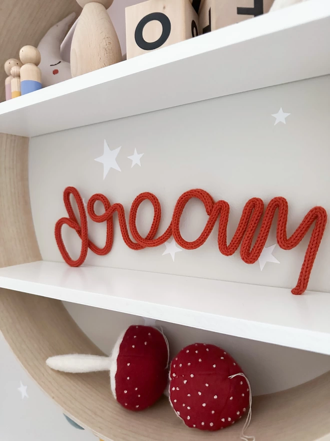 'dream' wooly word sign baby nursery decor propped up on a shelf.