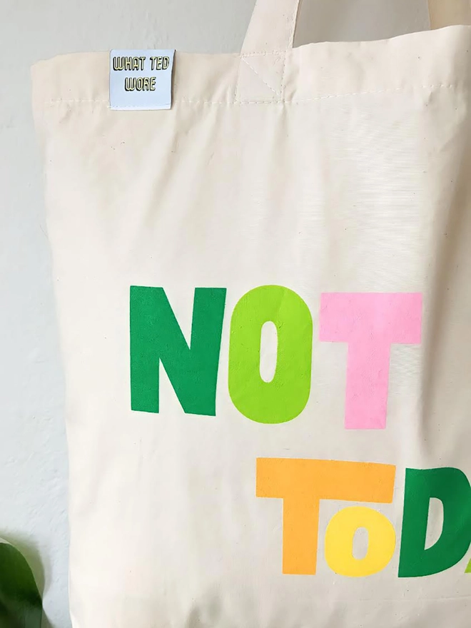 A hanging natural canvas tote bag with multi coloured Not Today slogan.