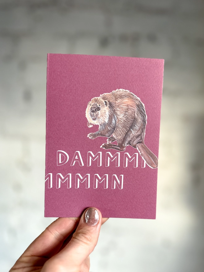 a pinky purple greetings card featuring an illustration of a beaver with the text “dammmmmn”
