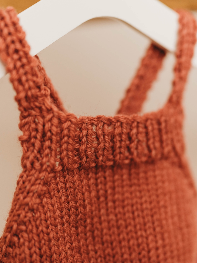 hand knitted personalised red teddy bear dungarees on toy hanger close up