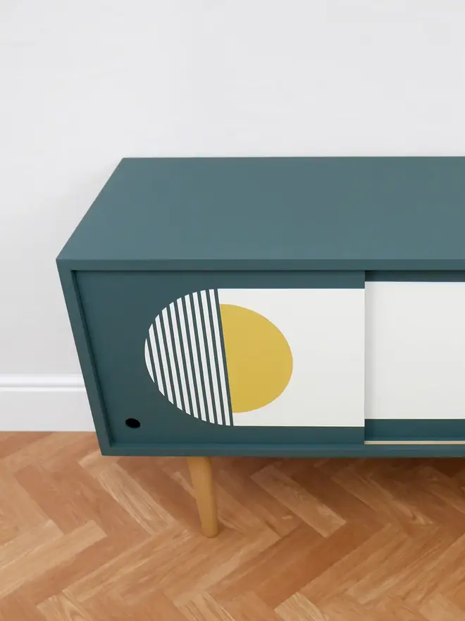 Teal mid-century record cupboard with sliding doors featuring bold geometric patterns in white and yellow.
