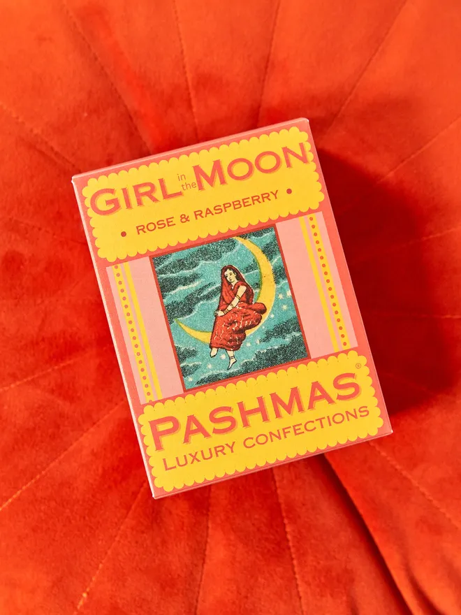 box of girl in the moon rose & raspberry sweets by pashmas, sitting on red cushion