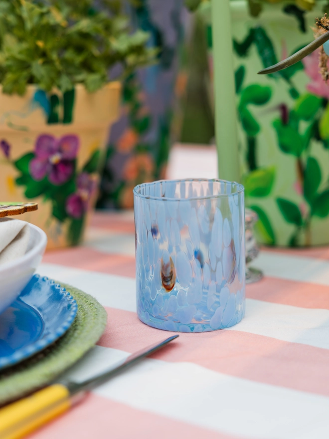 straight Murano style glass in Azzuro colour, on a spring tastemaker table surrounded by other colourful products such as cutlery and a striped tablecloth