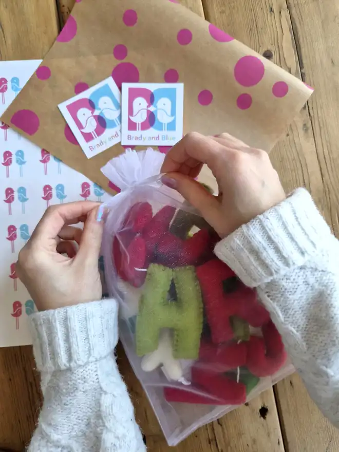 A 'Merry Christmas' felt garland in an organza gift bag, with gift wrapping and brand stickers.