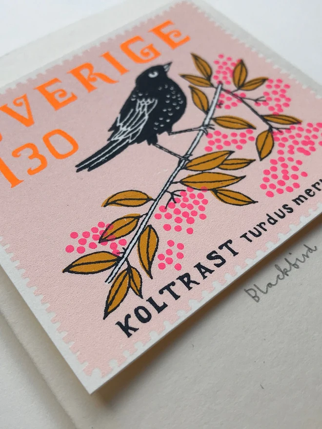 Bird Stamp Card Swedish/ Blackbird, a white card with a colourful bird design on a white backdrop. 
