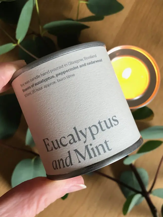 Eucalyptus & Mint Candle, held in a hand against a wooden background. 