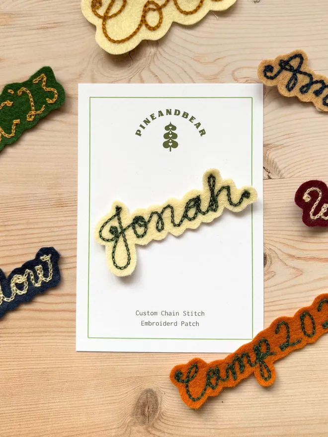 A selection of Personalised Chain Stitch name patches in various colours on a wooden background