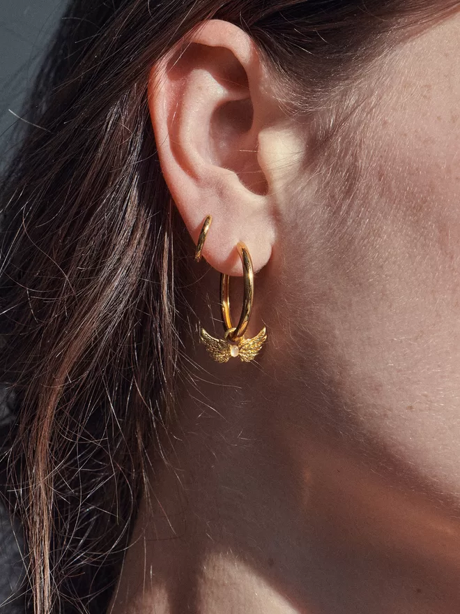 woman wearing a gold hoop with Hermes wings charm