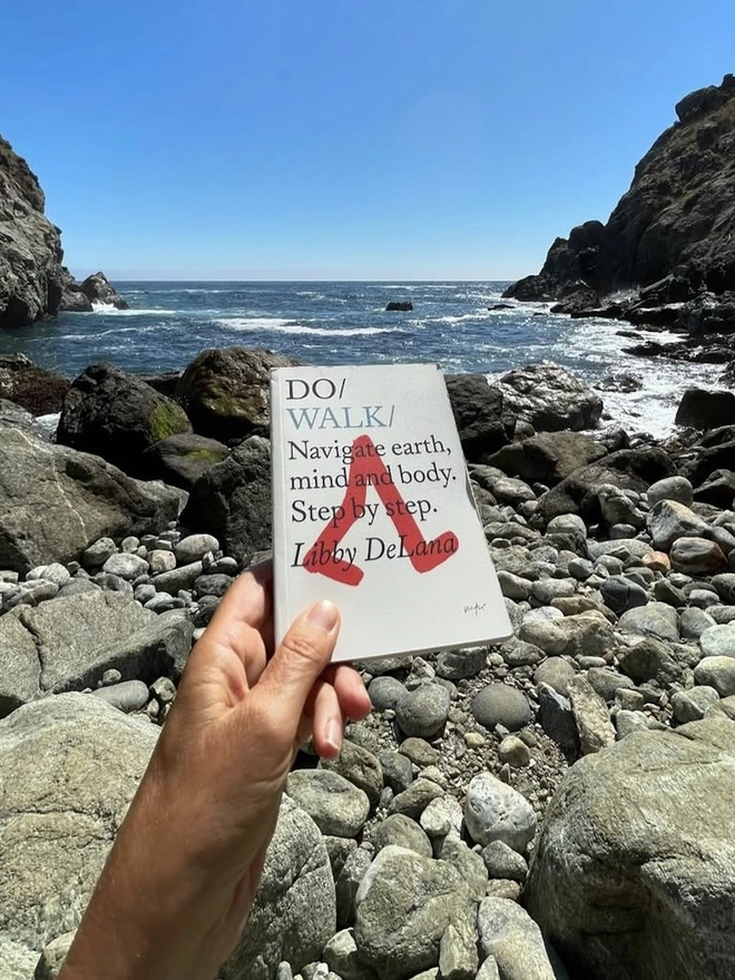 Book in woman's hand, held in front of sea and clear blue sky