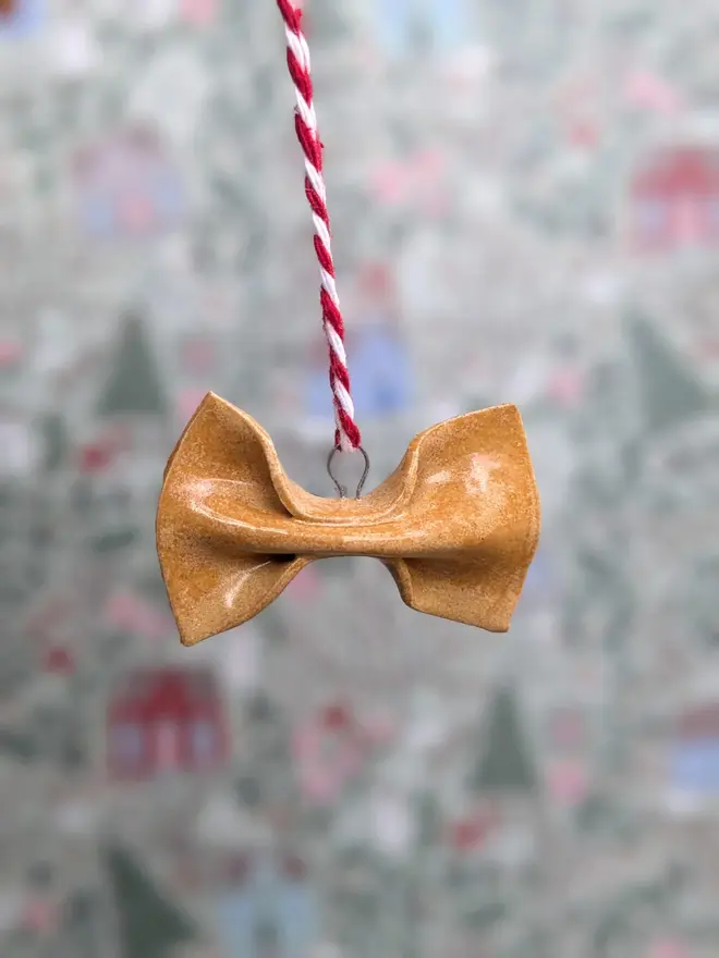ceramic farfalle christmas decoration. a small ceramic pasta decoration hanging from red and white thread.