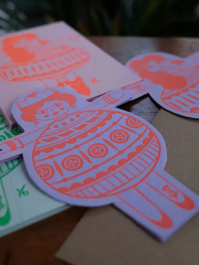 Illustrated ladies with bauble dresses – hand printed cut-out garland card in red ink on a light purple card.